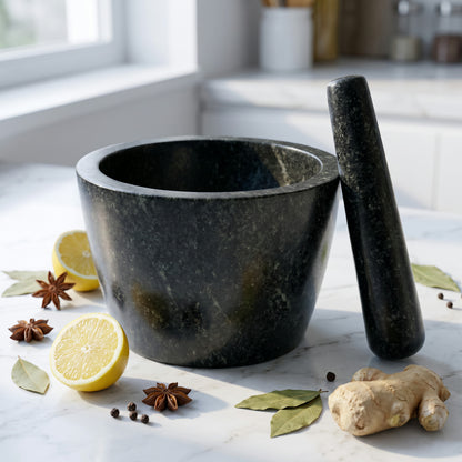 Round stone mortar and pestle in black Tamda stone placed on white marble kitchen counter
